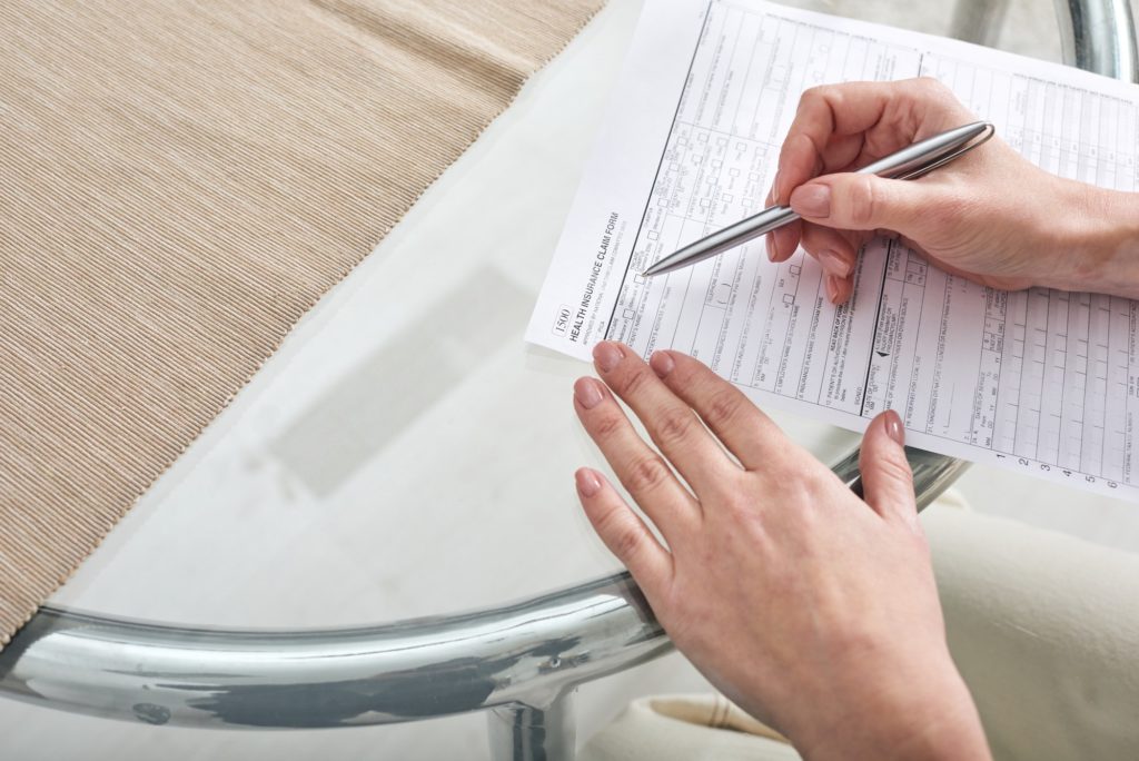 Hands of young female with pen over paper filling in health insurance claim form